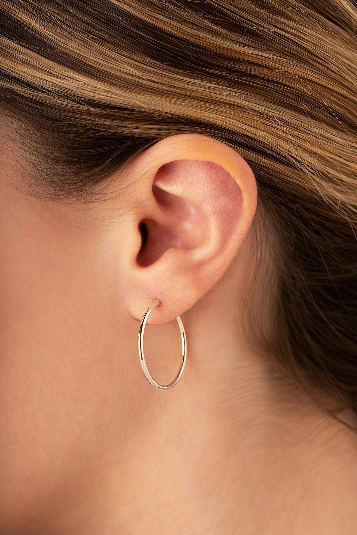 One inch polished tube hoop earring shown on the ear for size