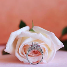 Load image into Gallery viewer, Kirk Kara White Gold &quot;Charlotte&quot; Pink Sapphire Emerald Cut Diamond Three Stone Engagement Ring Side View in Front Of Flower
