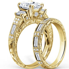 Load image into Gallery viewer, Kirk Kara Yellow Gold &quot;Charlotte&quot; Emerald Cut Three Stone Diamond Engagement Ring Set Angled Side View
