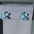 Load and play video in Gallery viewer, Gabriel &amp; Co. Lusso Blue Topaz and Diamond Flower Stud Earrings
